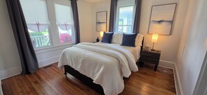 Um quarto com uma cama grande, duas mesas de cabeceira, uma janela com cortinas e obras de arte nas paredes.