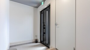A modern hallway with a light-colored floor, a dark door with a handle, and a small table with a metal frame.
