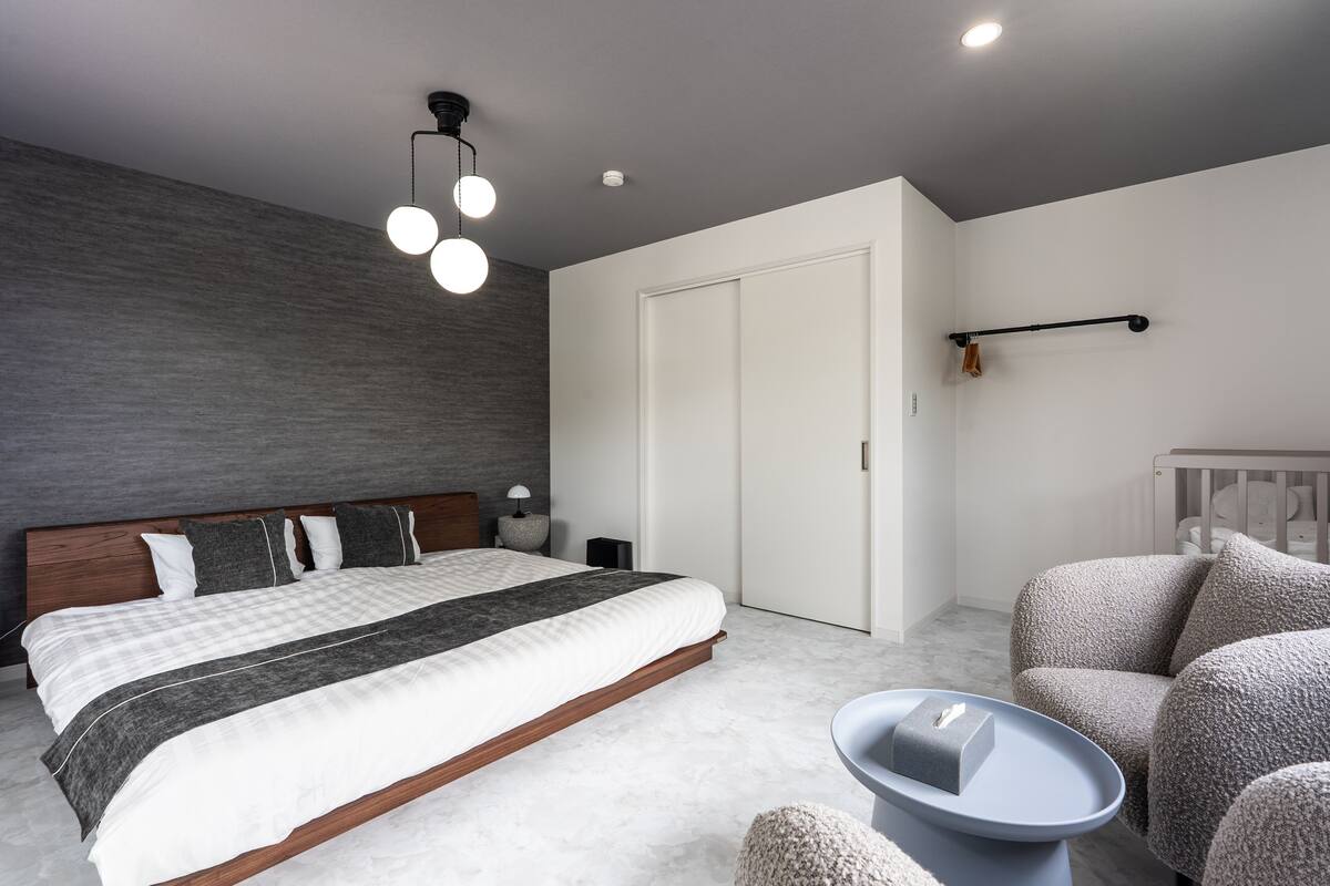 A modern bedroom with a large bed, a bedside table, a chair, and a small table with a box.