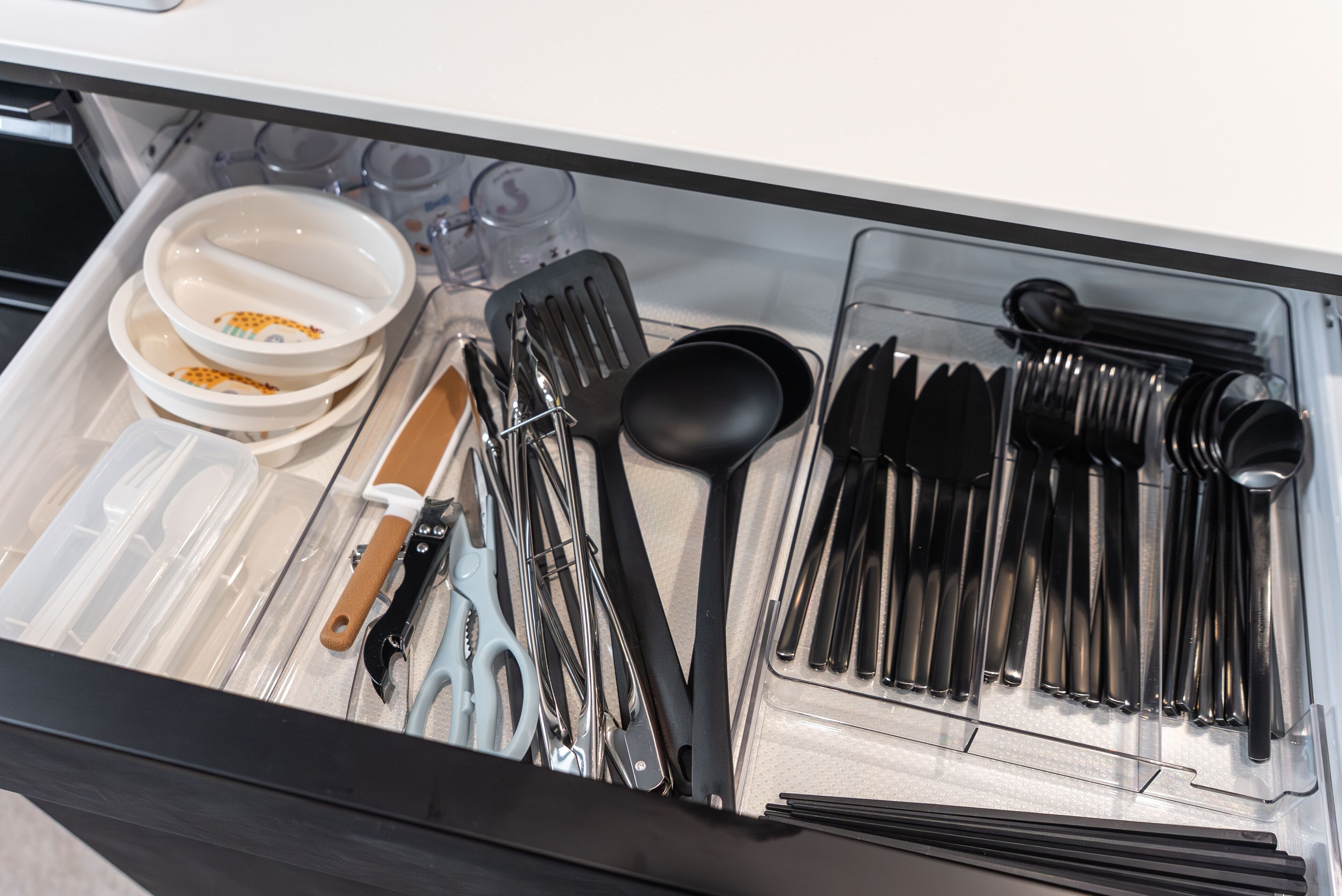 A drawer containing various kitchen utensils and dishes, including bowls, spoons, and a spatula.