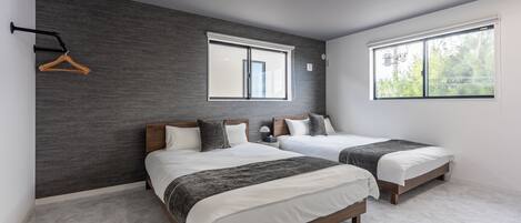 A modern bedroom with two beds, grey walls, and large windows.