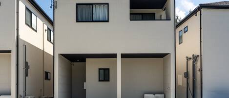 Un edificio residencial de dos pisos con fachada plana, ventanas grandes y un área de entrada cubierta.
