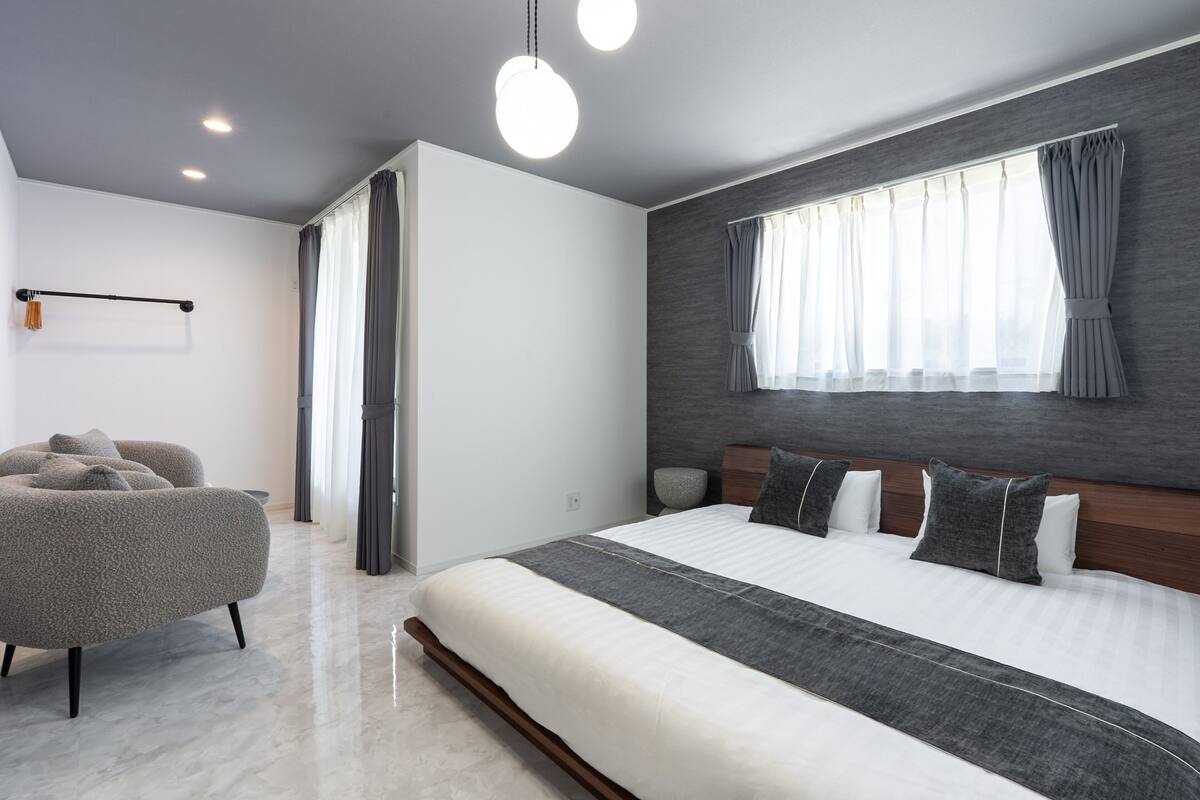 A modern bedroom with a large bed, a seating area, and a window with curtains.