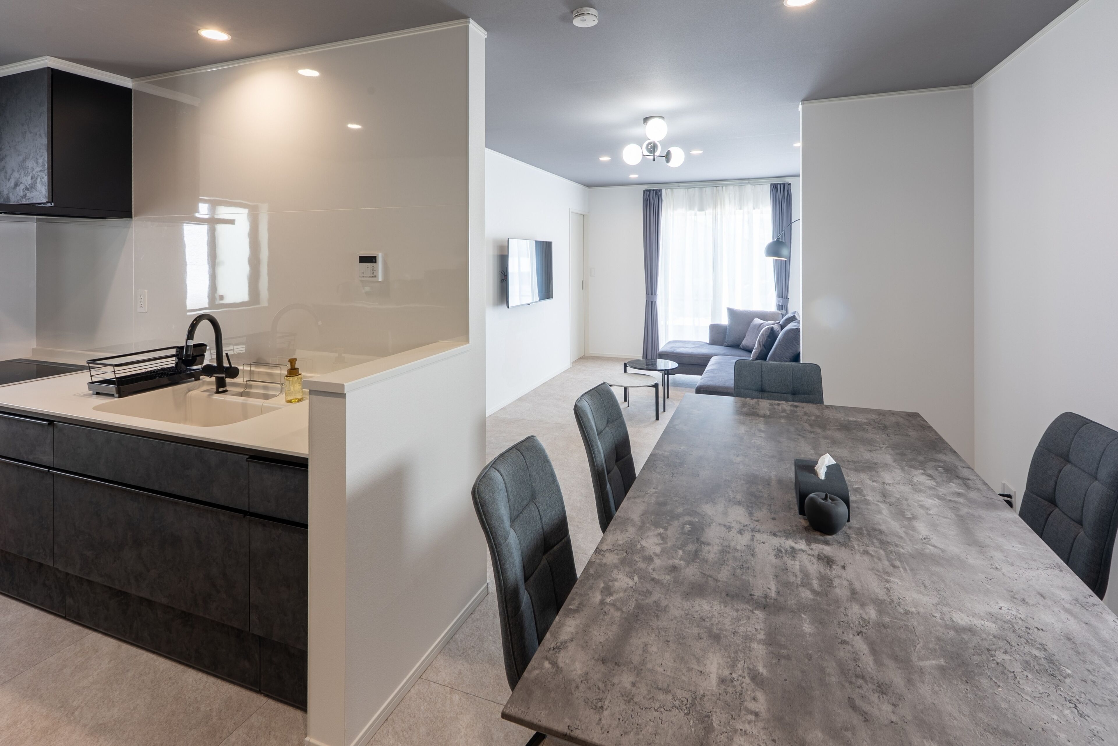 A modern kitchen with a large island, a dining area with a long table and chairs, and a living room with a sofa and a TV.