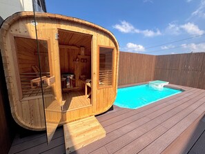 Una cabaña con jacuzzi de madera, con zona de estar integrada y una piscina pequeña.