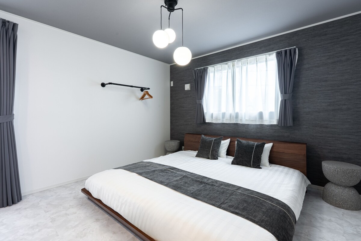 Un dormitorio moderno con una cama grande, un cabecero de madera, una mesita de noche, una lámpara colgante y una ventana con cortinas.