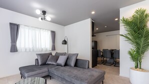 A modern living room with a grey sectional sofa, a glass coffee table, and a large potted plant.