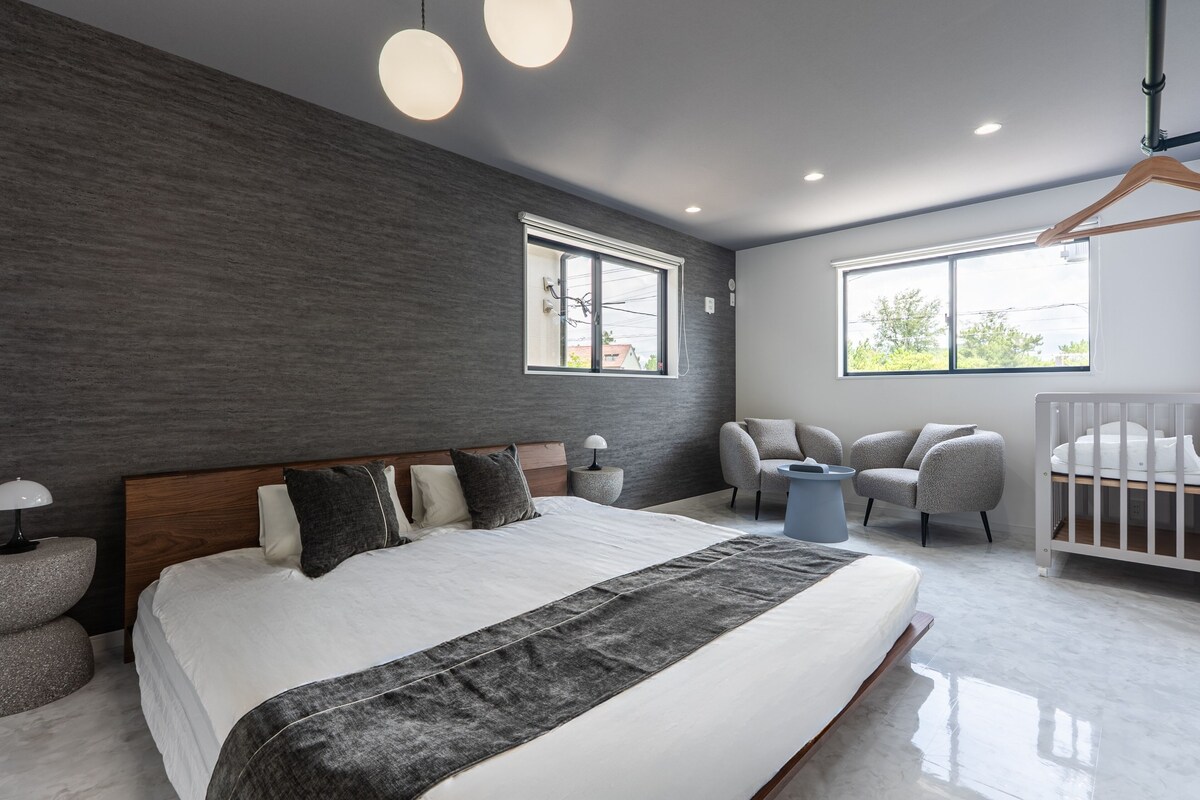 Un dormitorio moderno con una cama grande, dos ventanas, una cuna y una zona de estar.