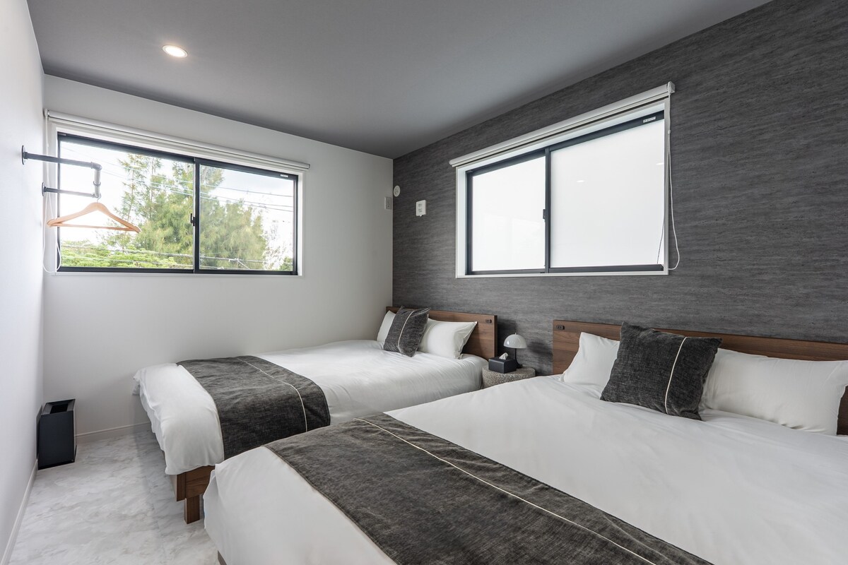 Una habitación de hotel moderna con dos camas, un ventanal grande y una pared de acento gris.