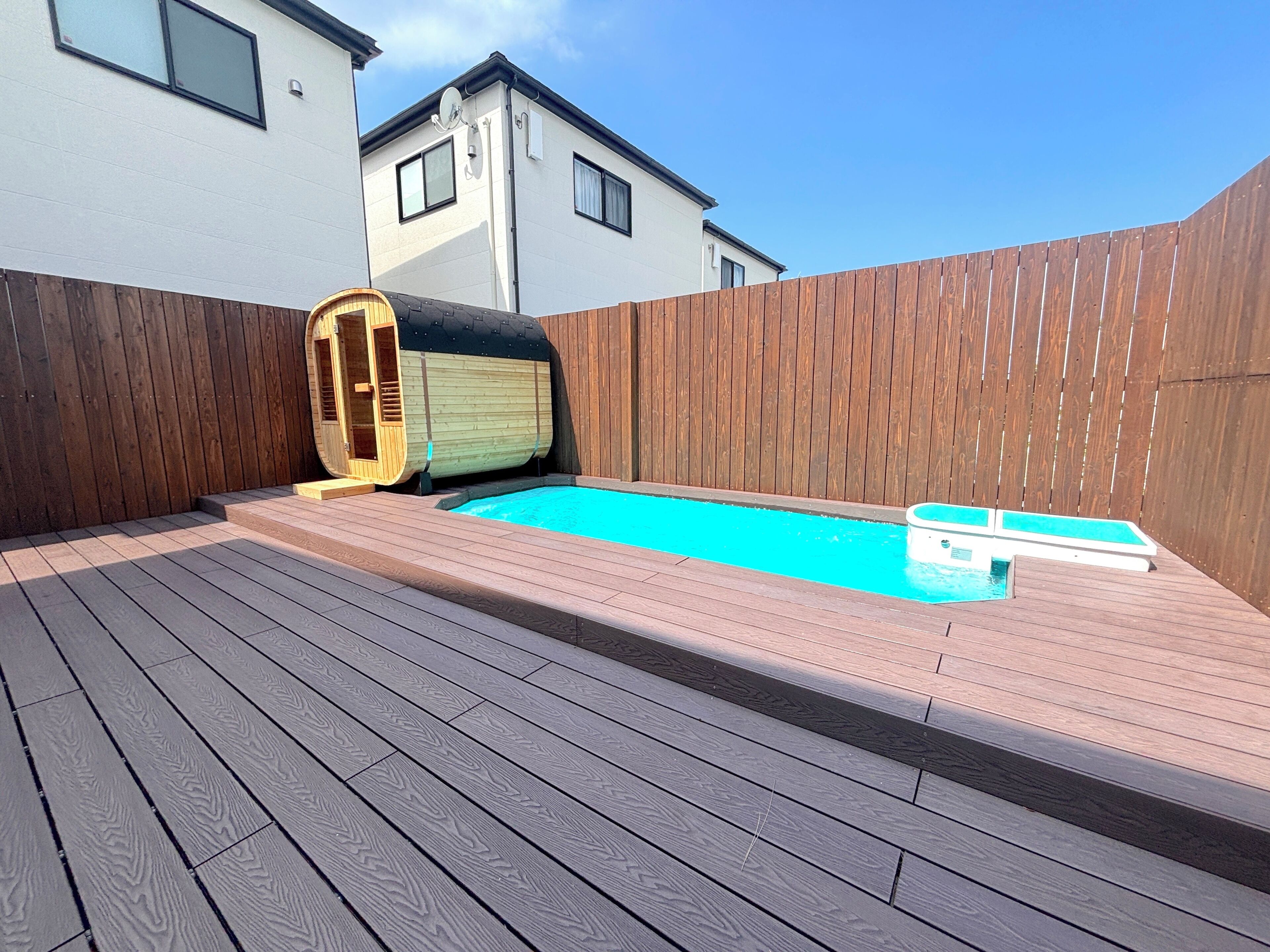 Piscina com deck de madeira, sauna e cerca de madeira.