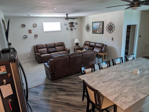 A spacious living room with a brown leather sectional sofa, a dining table with chairs, a ceiling fan, and decorative wall art. - Rally Oasis, Quieter neighborhood, Walking distance to Main Street (Sturgis)