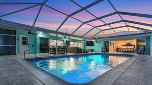 Una piscina interior con techo de vidrio, un área de descanso y un dormitorio con cama y televisor.