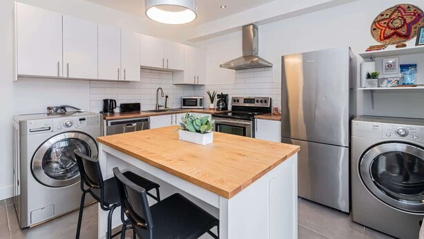 Een moderne keuken met roestvrijstalen apparatuur, een houten kookeiland en een ingebouwde wasmachine.