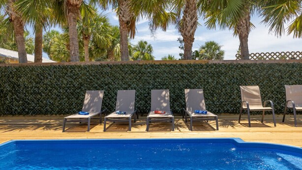 Una piscina con sillones de descanso y palmeras al fondo.