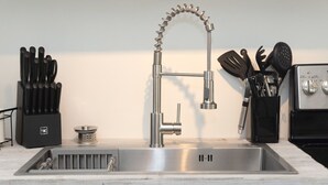 Una cocina con un lavamanos de acero inoxidable, un grifo moderno y diversos utensilios organizados en recipientes.