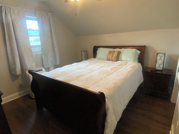 A bedroom with a bed, a window with curtains, a nightstand, and a wall-mounted light fixture.