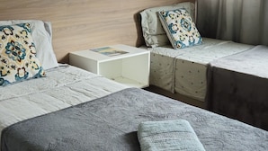 Une chambre à coucher avec une tête de lit en bois, deux lits avec une literie à motifs, une table de chevet avec une lampe et une fenêtre avec des rideaux.