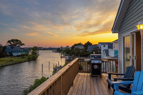 Une terrasse en bois avec un barbecue et des chaises, donnant sur une rivière.