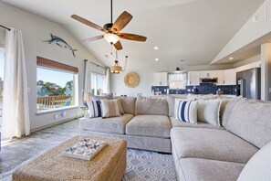 Un salon moderne avec un canapé d’angle, un ventilateur de plafond et une vue sur l’extérieur.
