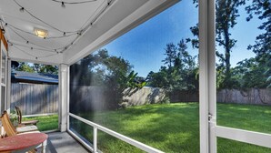 A covered patio with a view of a grassy backyard, a wooden table, and chairs.