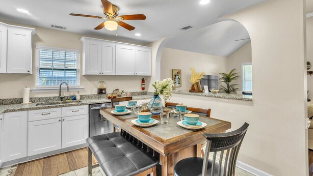 A modern kitchen with white cabinets, a granite countertop, and a dining area with a wooden table and black chairs.