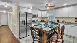A modern kitchen with white cabinets, stainless steel appliances, and a wooden dining table with blue and white bowls.