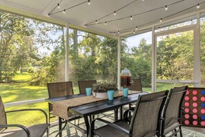 A covered patio with a table set for four, surrounded by chairs, and a large window offering a view of a lush garden.