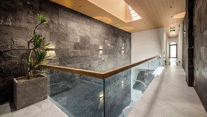 Un interior moderno con pared de piedra, techo de madera y barandilla de vidrio con vista a un nivel inferior.
