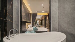 Un baño moderno con una bañera grande, un espejo y una cama visible a través de una pared de vidrio.