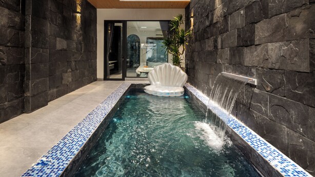 Una piscina interior moderna con un llamativo borde de mosaico azul, una cascada central y techo de madera.