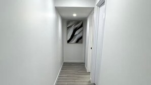 A hallway with a wooden floor, white walls, and a ceiling light.