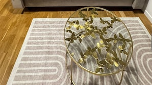 A living room with a grey sofa, a glass coffee table with gold accents, and a patterned rug.