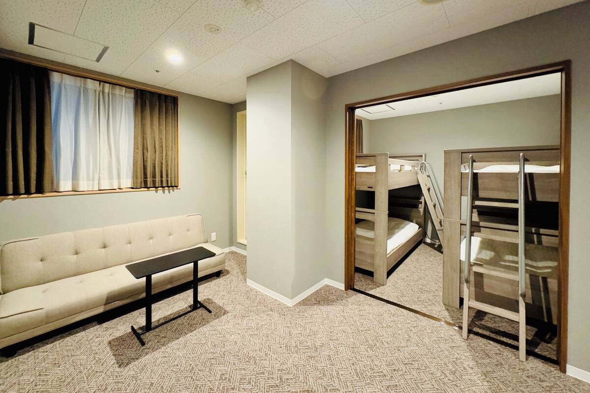 A hotel room with a sofa, a small table, a bunk bed with a ladder, and a carpeted floor.