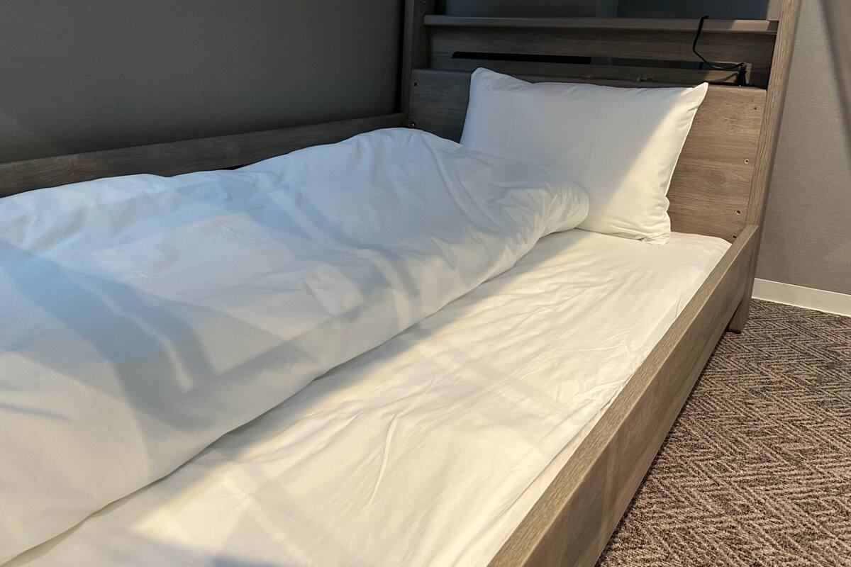 A single bed with white bedding in a room with a wooden headboard and a patterned carpet.