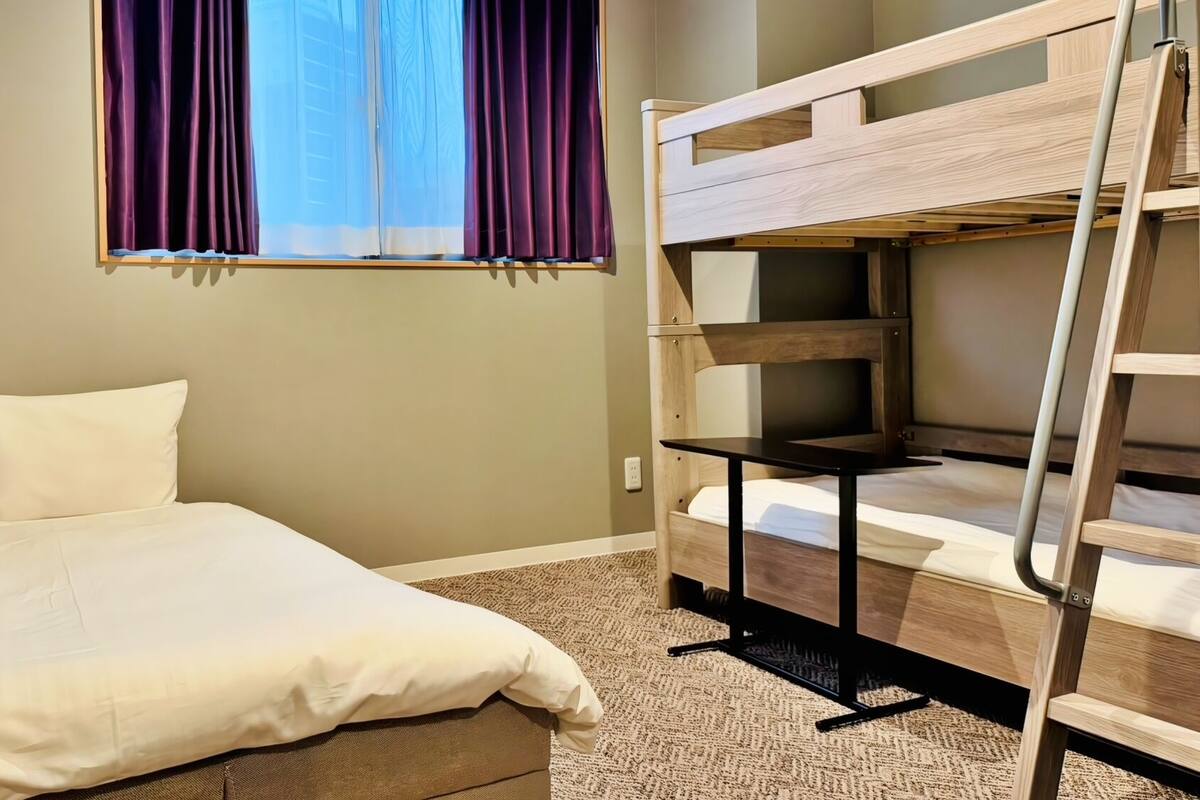 A bunk bed with a desk, a single bed, and a window with curtains.
