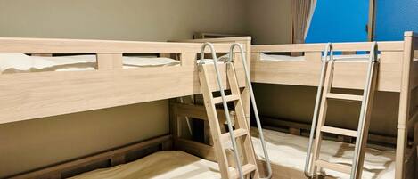 A bunk bed room with wooden frames, metal ladders, and a window with curtains.