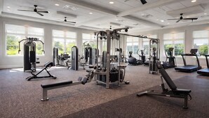 Un gimnasio con diversas máquinas de ejercicio, amplias ventanas y ventiladores de techo.