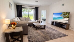 Una sala moderna con sofá, mesa de centro, televisor y vistas al exterior.