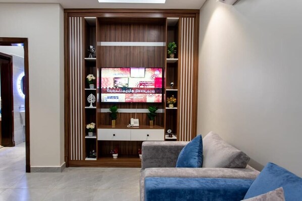 A living room with a TV on a wooden entertainment unit, a sofa, and decorative items.
