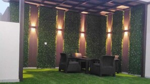 Un espacio de estar al aire libre cubierto con una pérgola, un muro verde e iluminación ambiental.