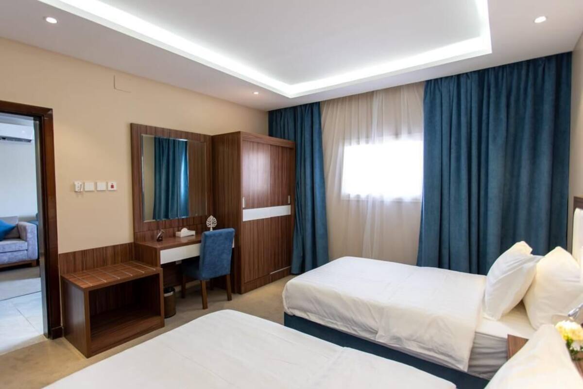Habitació d'hotel amb dos llits, un escriptori, una cadira, un mirall i un armari.