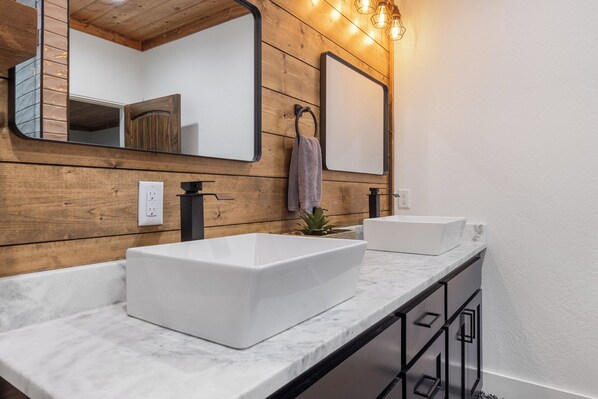 Une salle de bain avec deux lavabos blancs, des murs recouverts de panneaux en bois, un grand miroir et une serviette accrochée au mur.