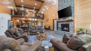 A spacious living area with leather sofas, a stone fireplace, and a high ceiling with wooden beams.