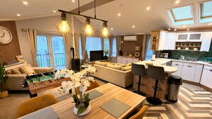 Un salon moderne avec un canapé, une table basse et un baby-foot. On y trouve également un coin repas avec une table et des chaises, ainsi qu’une cuisine équipée d’un comptoir et de placards.