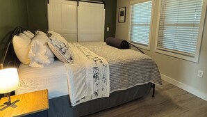Een slaapkamer met een bed, nachtkastje, plafondventilator en een raam met zonwering.