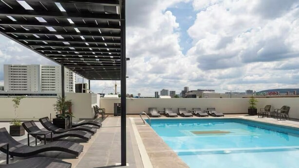 Un área de piscina en la azotea con sillones de descanso y una pérgola.