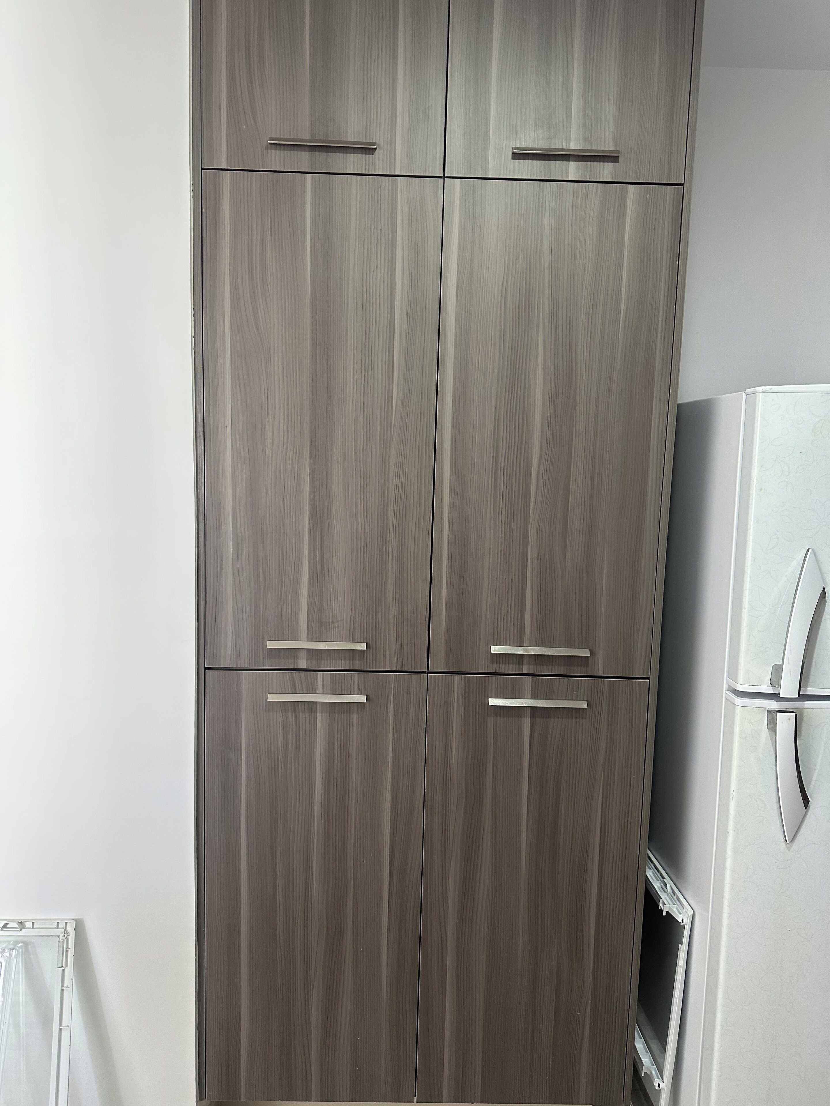 Une armoire à quatre portes avec des poignées, un réfrigérateur blanc orné d’un motif, et une fenêtre avec des stores.