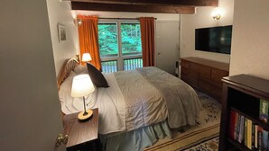 Un dormitorio con cama, lámpara de noche, televisor y estantería.