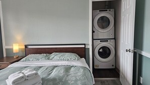 A hotel room with a bed, a washing machine, and a nightstand with a lamp. - Apartment Close to Hospital and UAA (Anchorage)
