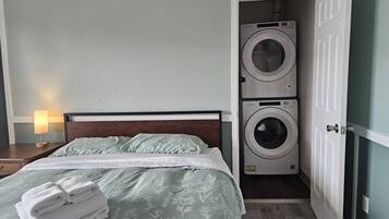 Una habitación de hotel con una cama, una lavadora y una mesita de noche con una lámpara.